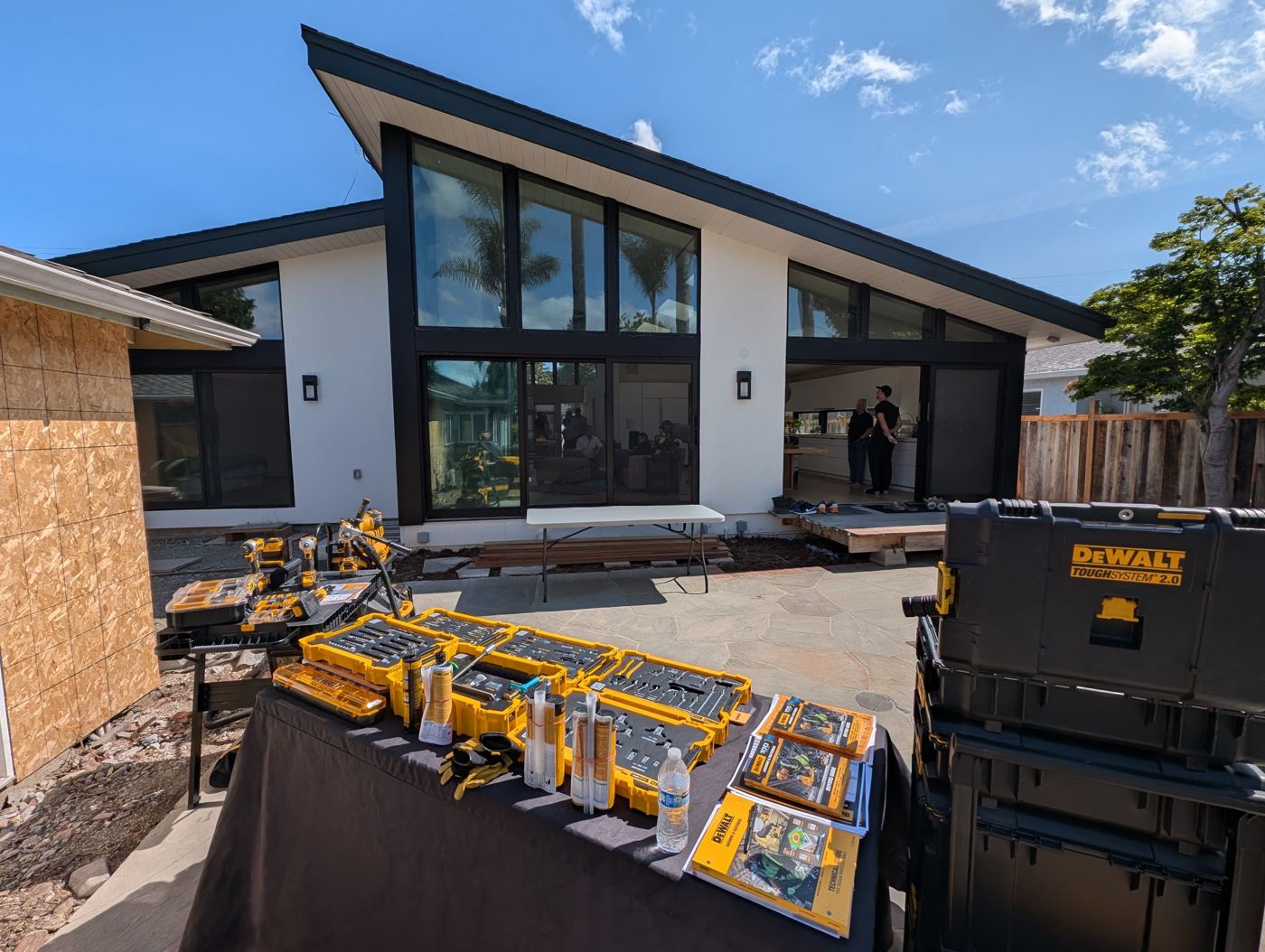Modern home exterior with tall angled windows and DeWalt demo tables on the patio